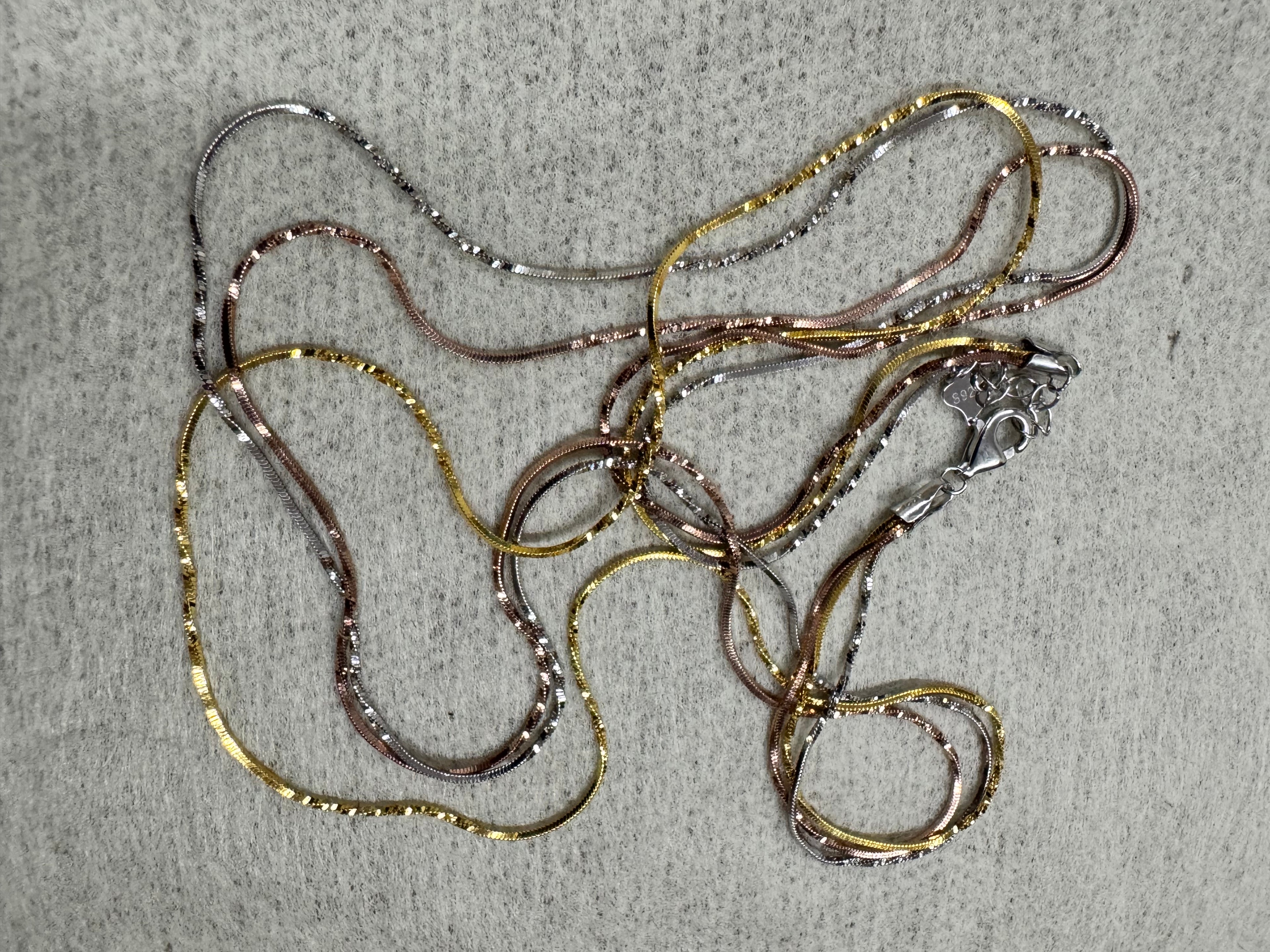 Tri-tone sterling silver three-strand snake chain necklace laid out full length on grey felt, 50 cm, with its lobster clasp.
