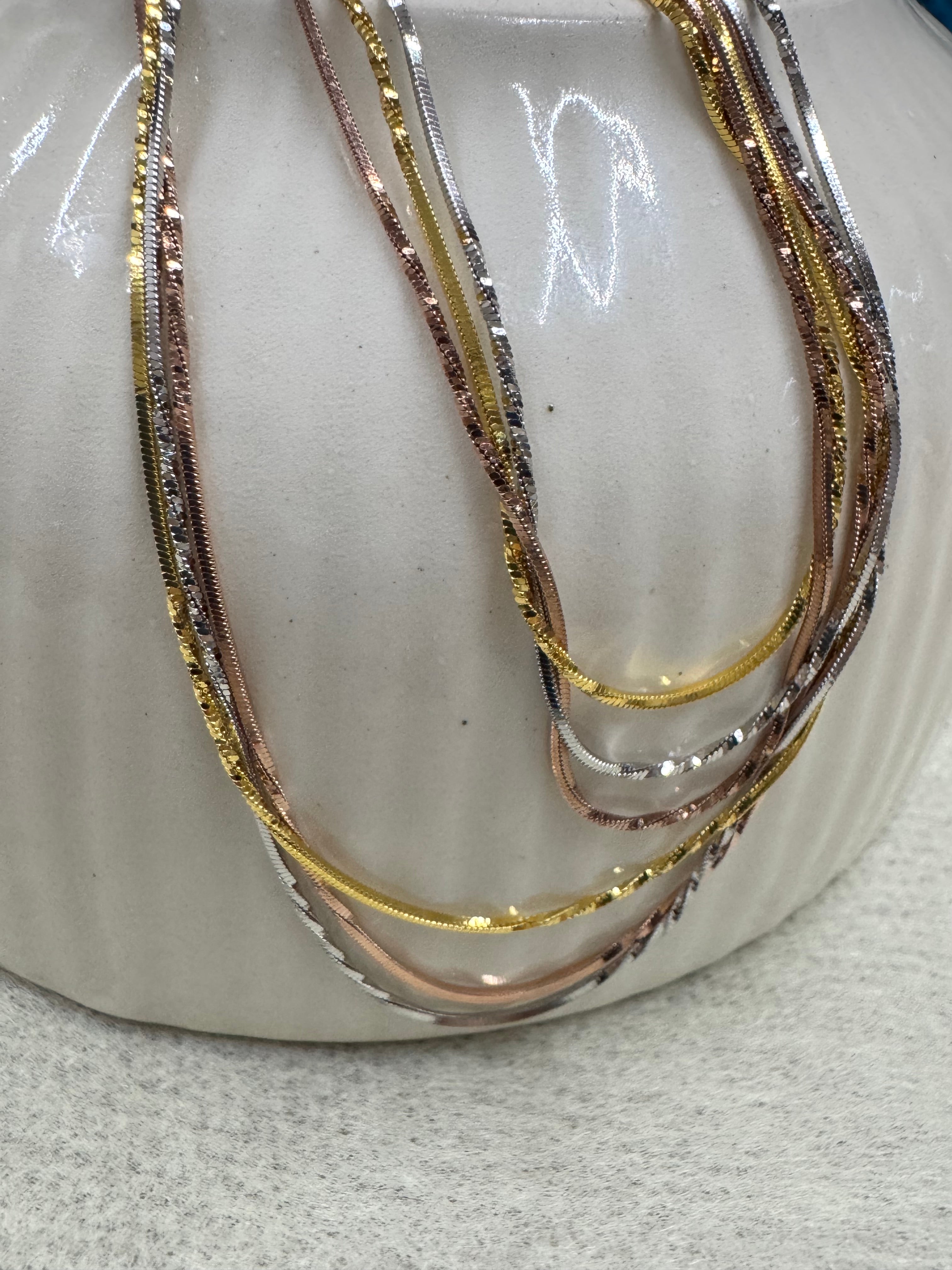 Silver, gold-tone and rose-tone strands of the sterling silver snake chain necklace draped over a pale stone dish.