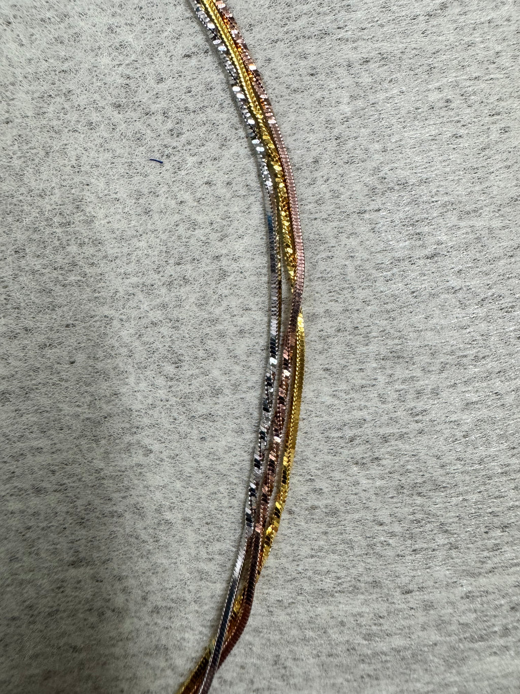 The three strands of the sterling silver snake chain necklace lying side by side in a shallow arc on grey felt.