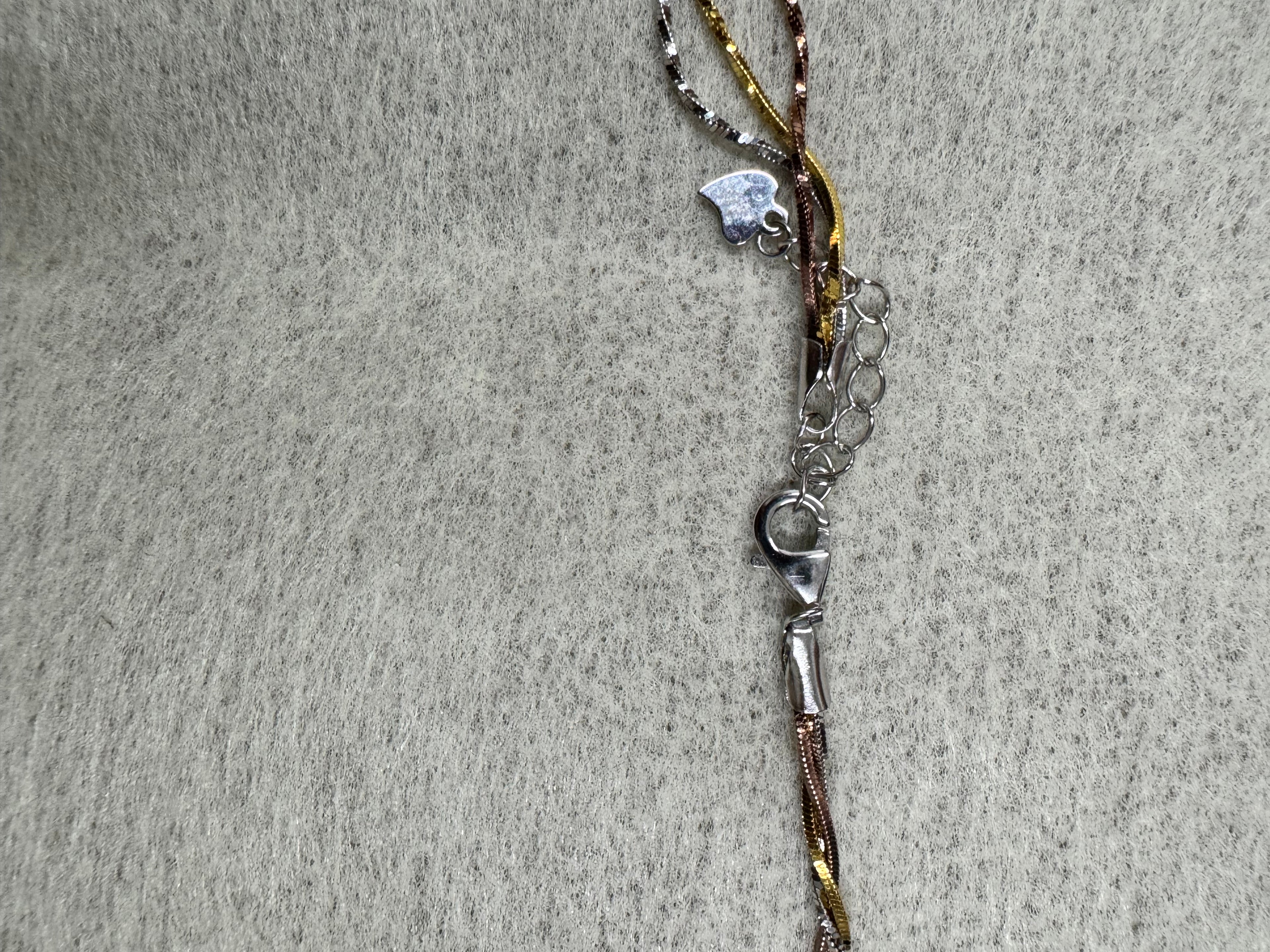 Lobster clasp, extender chain and small heart charm at the fastening of the sterling silver three-strand necklace.