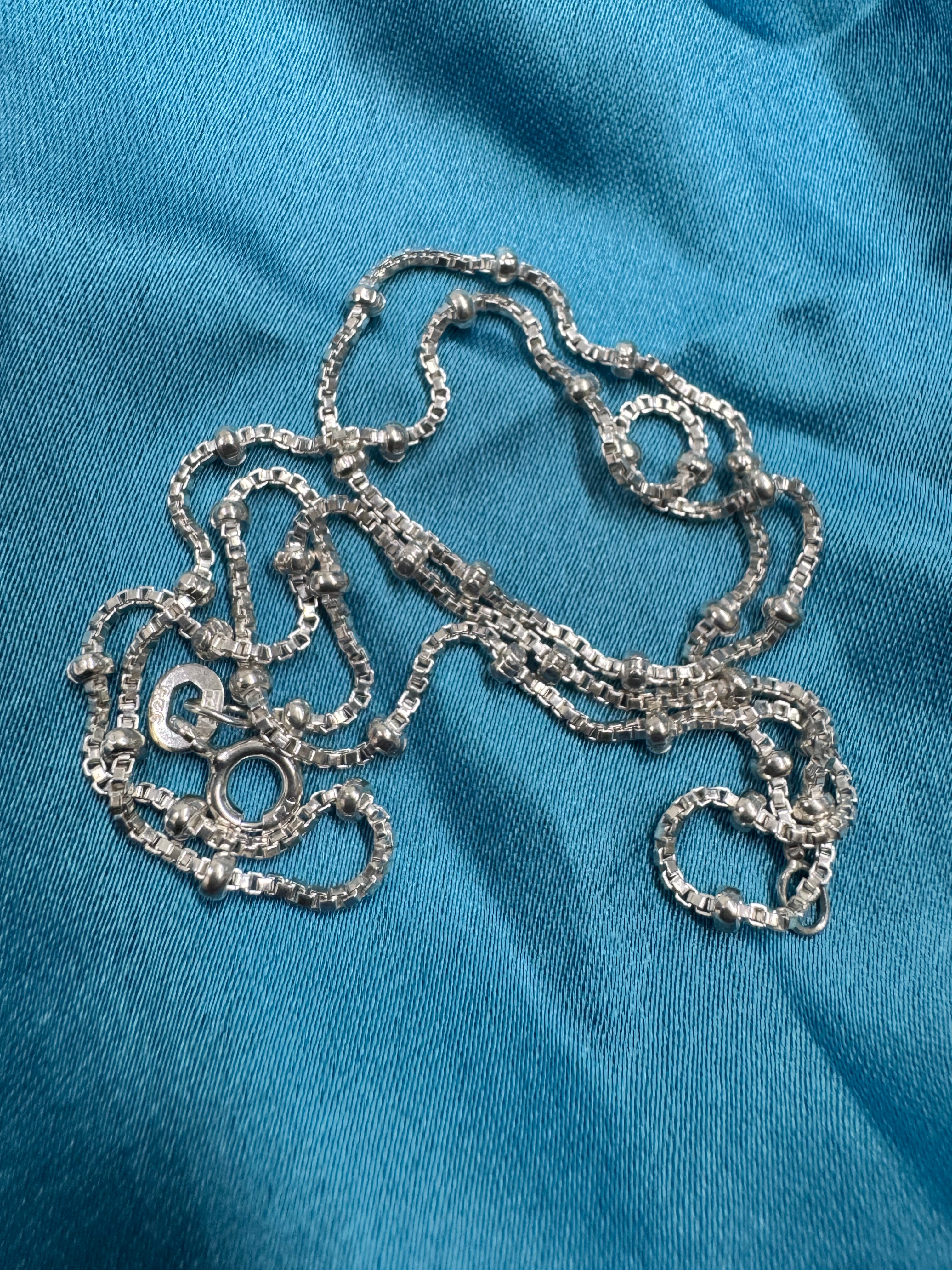 Sterling silver satellite box chain necklace coiled on blue satin, with the spring ring clasp visible.