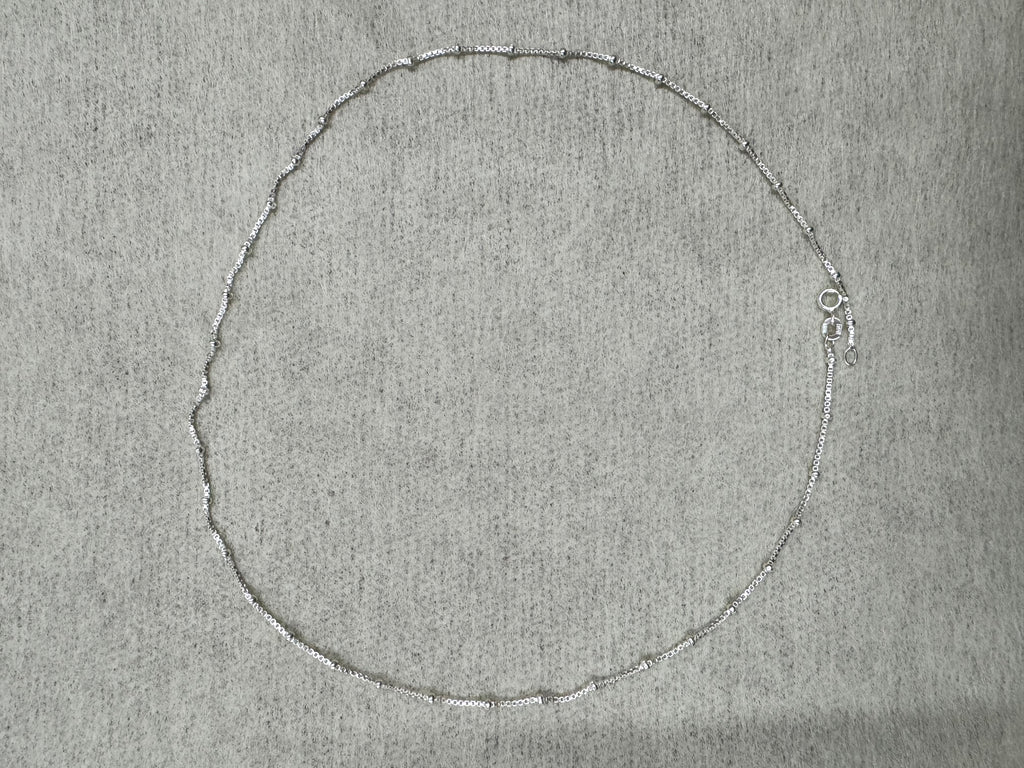 The 45 cm sterling silver box chain necklace laid out in a full circle on grey felt.