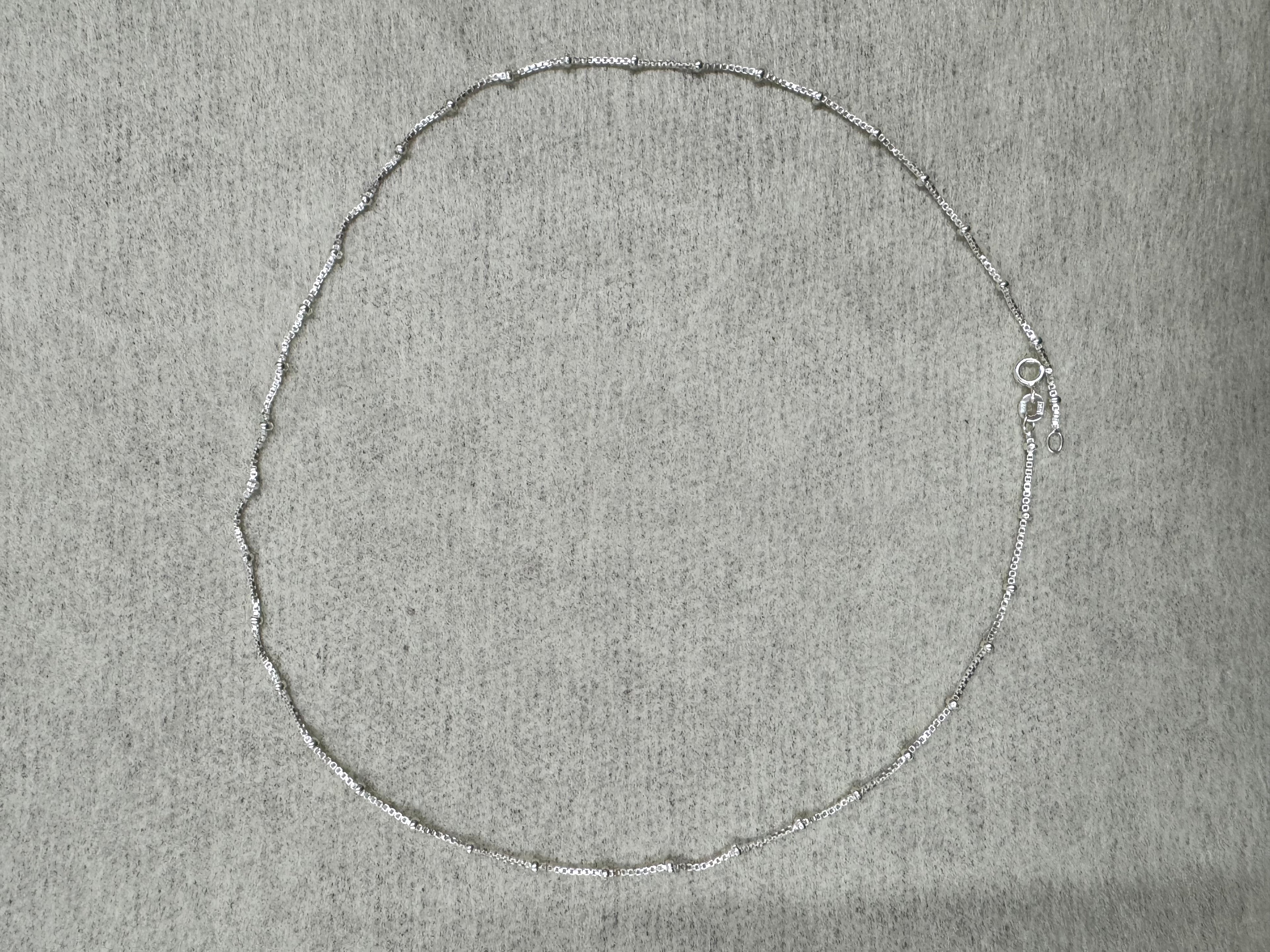 The 45 cm sterling silver box chain necklace laid out in a full circle on grey felt.