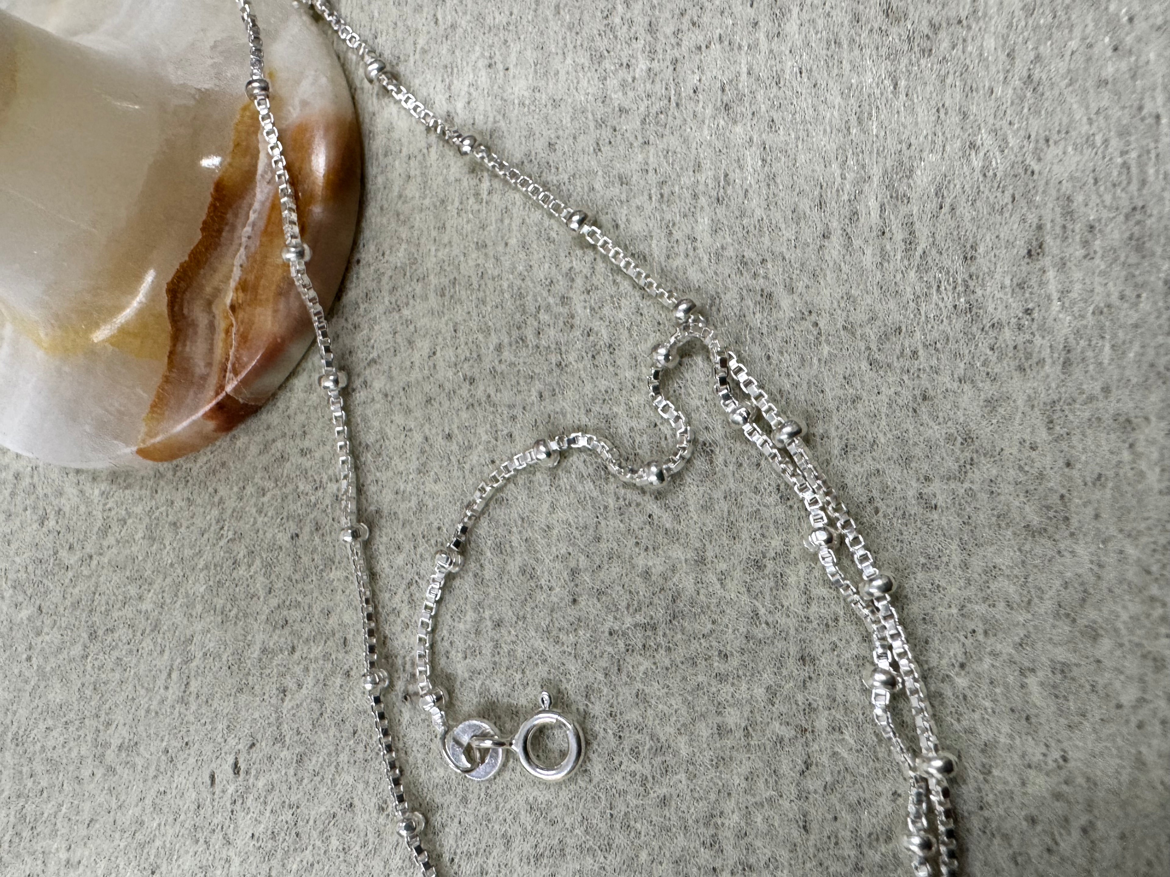 Spring ring clasp of the sterling silver satellite box chain necklace beside a banded onyx stone.