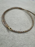 Tri-tone sterling silver twisted rope chain choker laid in a circle on grey felt, with its lobster clasp at the front.