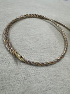 Tri-tone sterling silver twisted rope chain choker laid in a circle on grey felt, with its lobster clasp at the front.