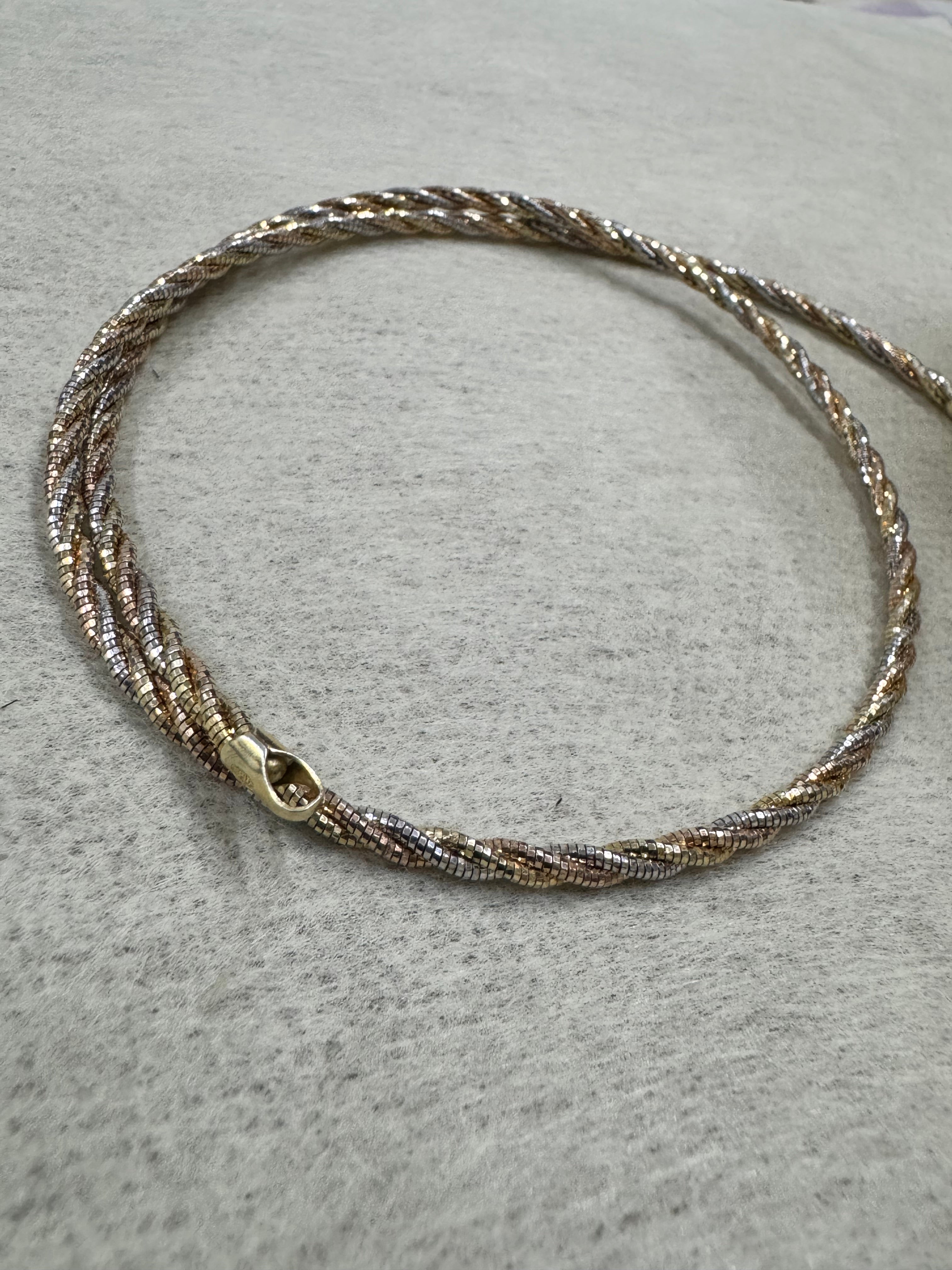 Tri-tone sterling silver twisted rope chain choker laid in a circle on grey felt, with its lobster clasp at the front.