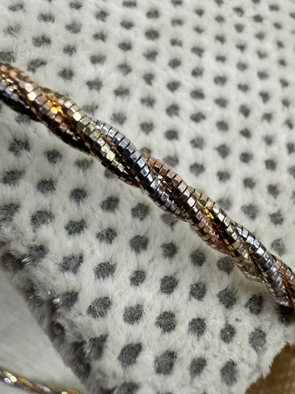 Macro view of the diamond-cut facets on the twisted sterling silver chain necklace, against spotted grey fabric.