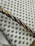 Macro view of the diamond-cut facets on the twisted sterling silver chain necklace, against spotted grey fabric.