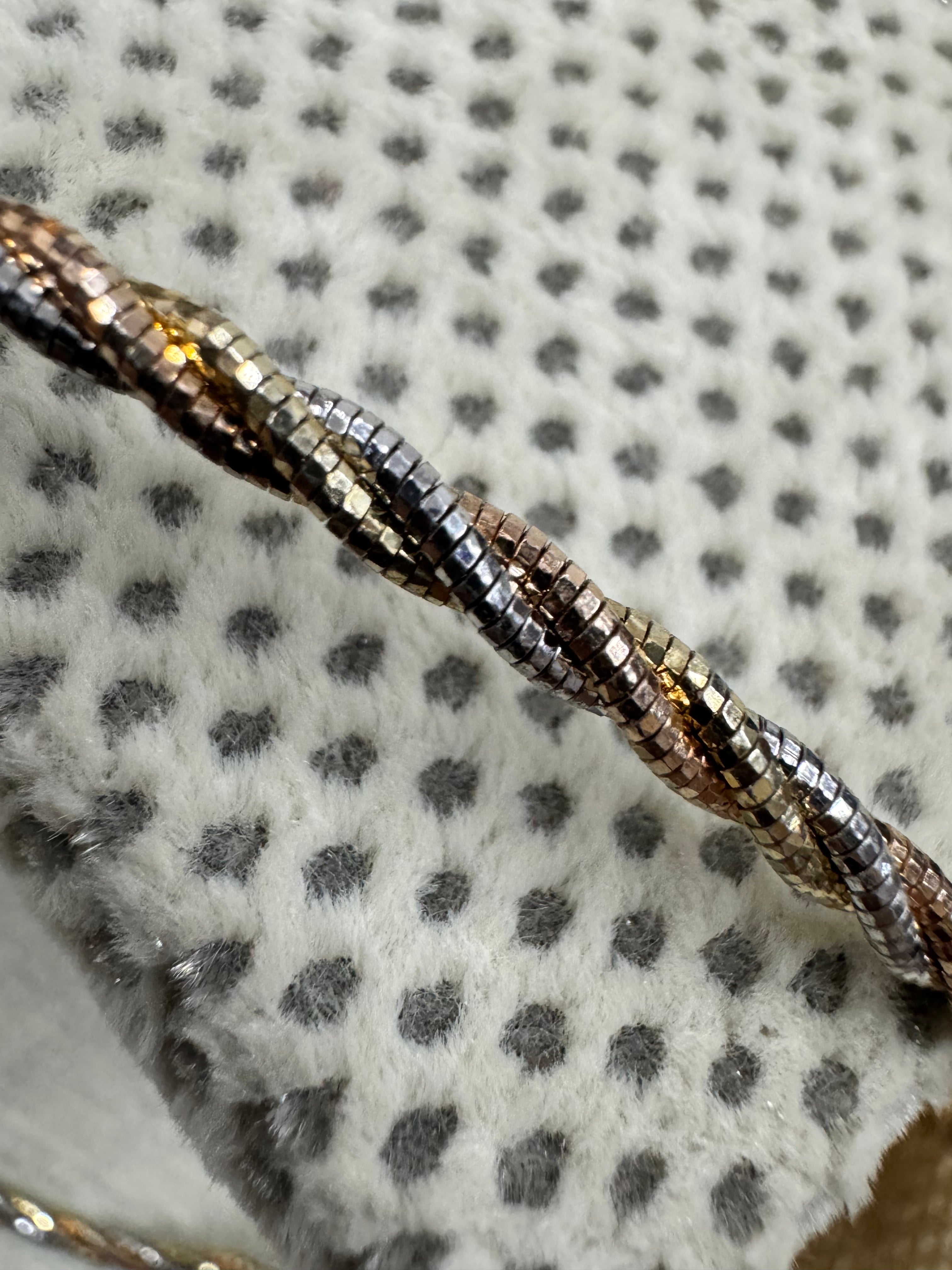 Macro view of the diamond-cut facets on the twisted sterling silver chain necklace, against spotted grey fabric.
