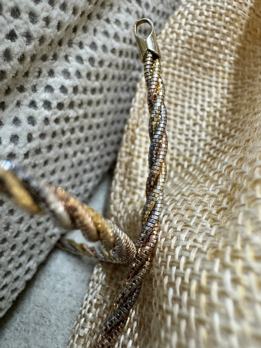 Tapered end cap and loop of the tri-tone sterling silver rope chain necklace resting on woven jute.