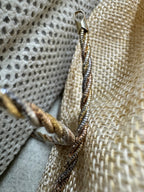 Tapered end cap and loop of the tri-tone sterling silver rope chain necklace resting on woven jute.