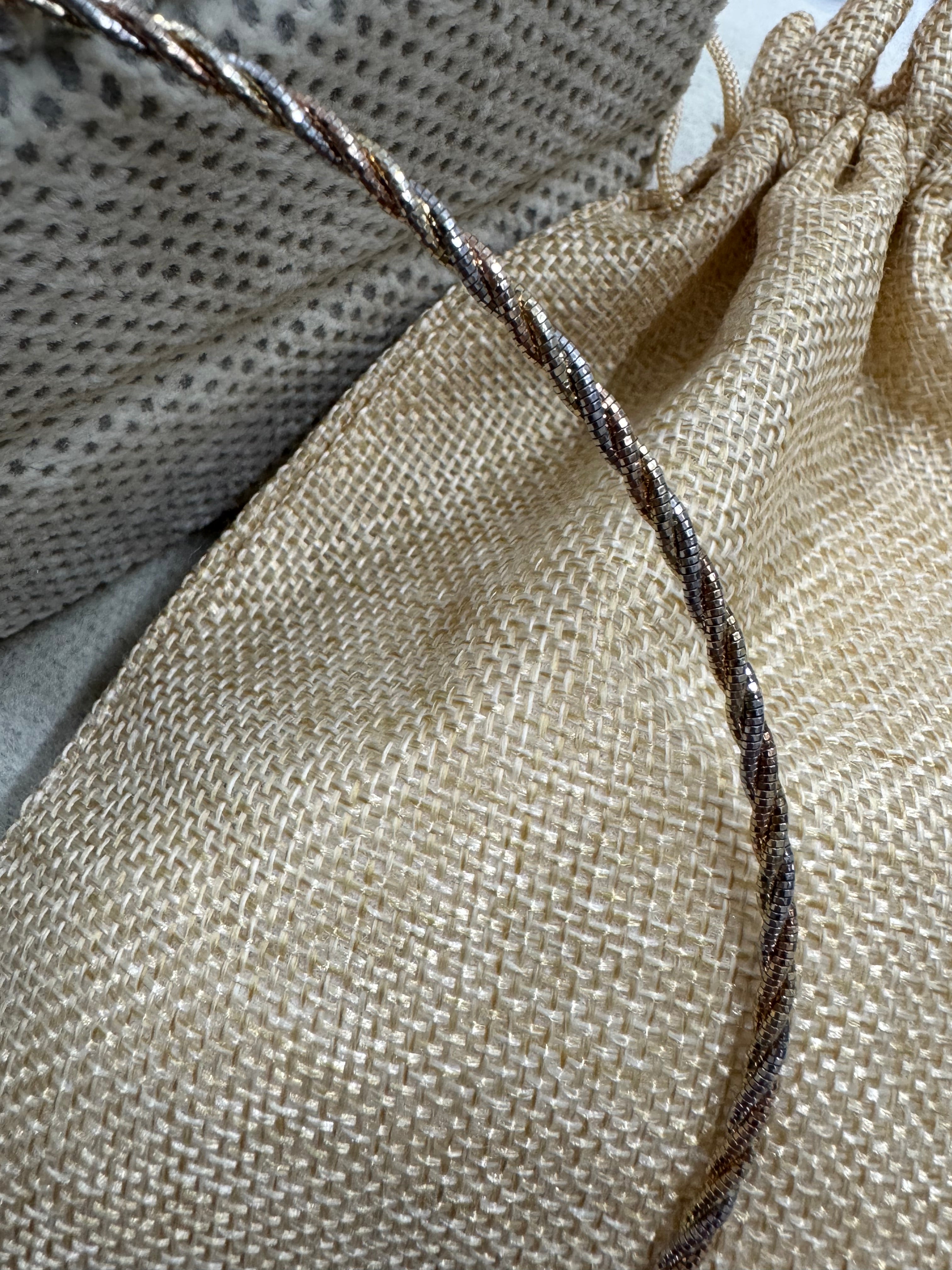 The sterling silver twisted rope chain necklace curving across a jute drawstring pouch.