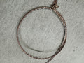 Rose-tone sterling silver snake chain choker laid in a circle on grey felt, clasp at the front.