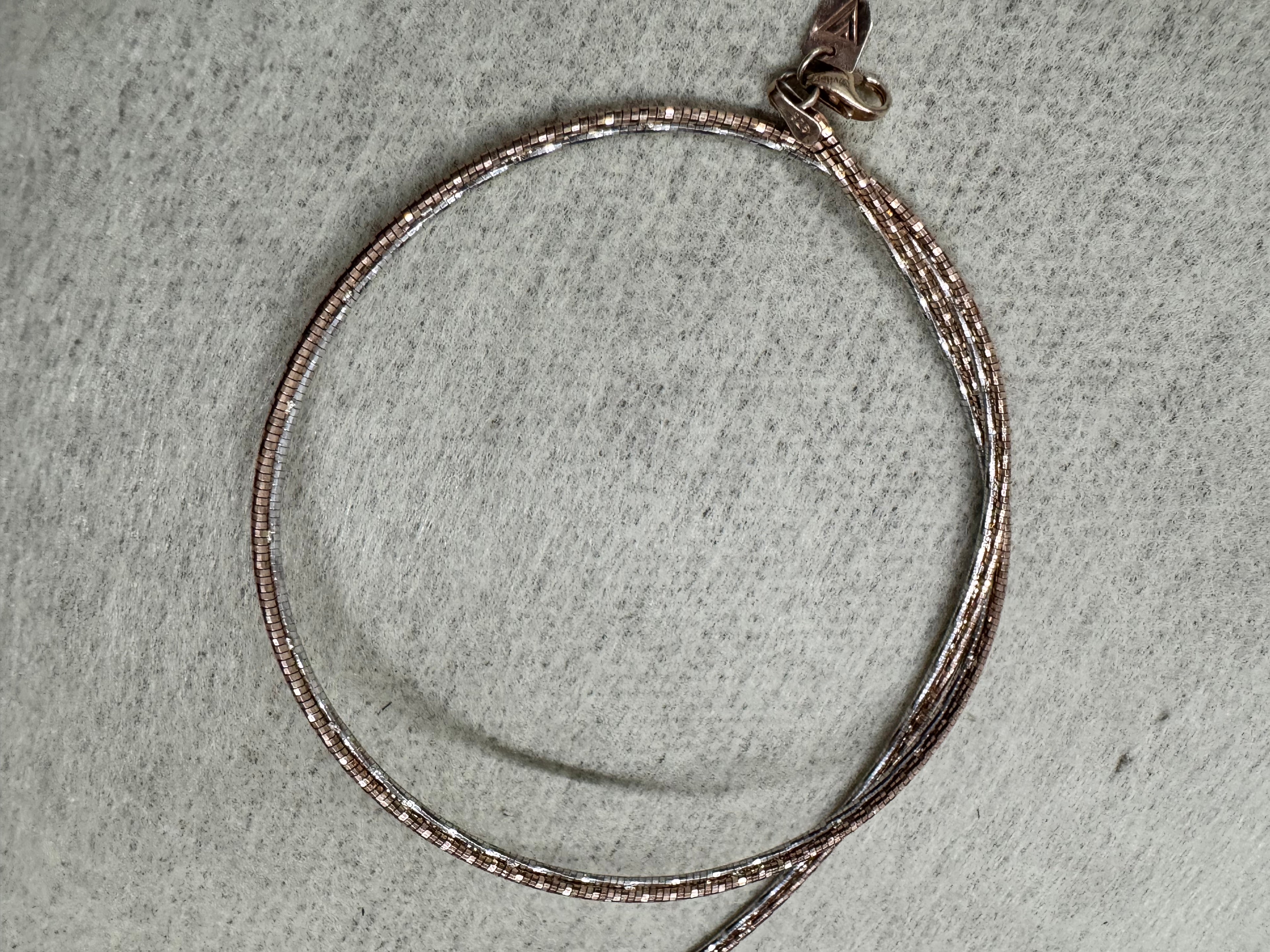 Rose-tone sterling silver snake chain choker laid in a circle on grey felt, clasp at the front.