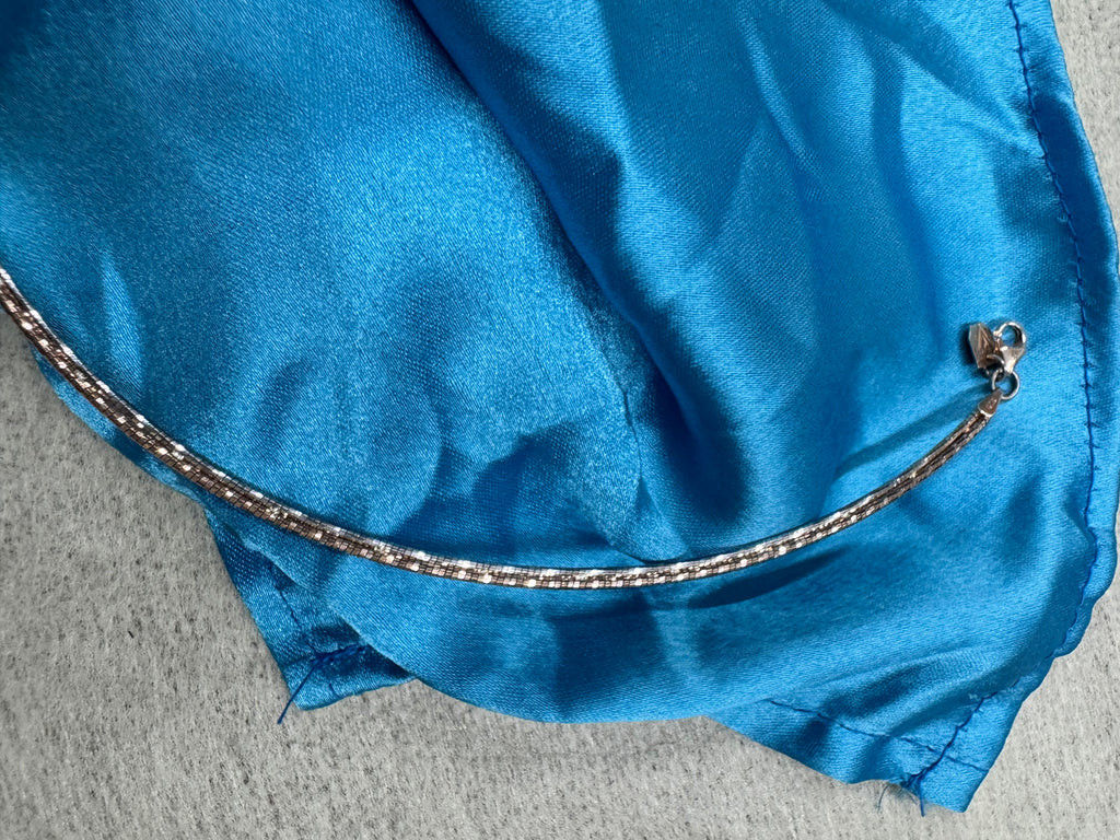 Rose-tone sterling silver snake chain necklace resting on blue satin, with the lobster clasp at the left.
