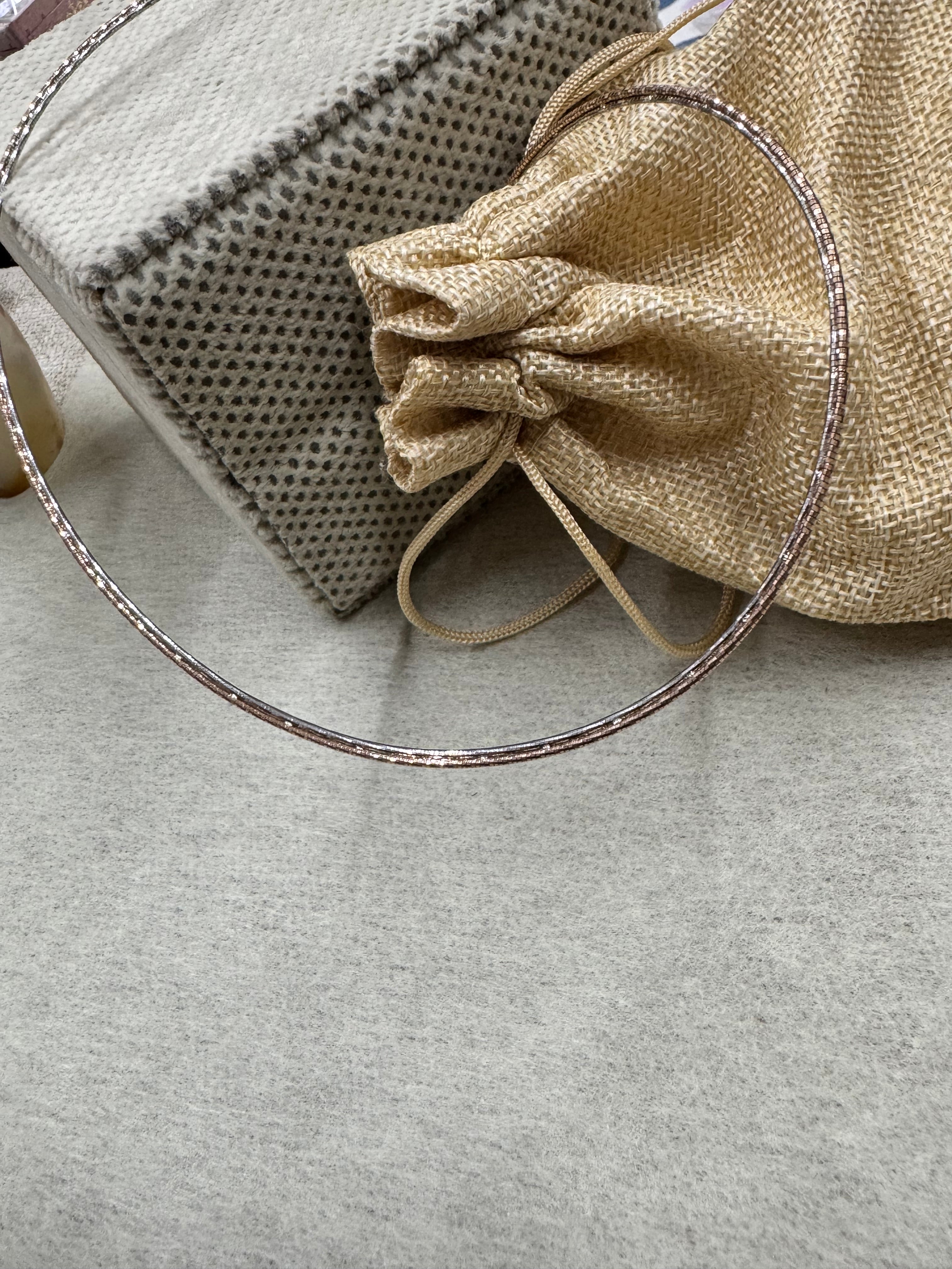 The 45 cm sterling silver snake chain necklace laid beside a jute drawstring pouch and folded fabric.