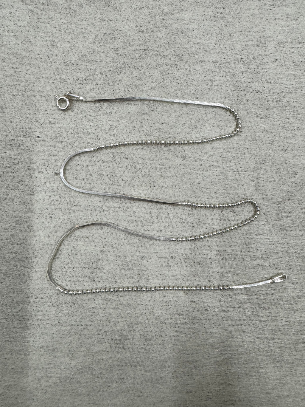 Full 45 cm length of the sterling silver chain necklace laid out on grey felt, showing snake sections alternating with runs of round beads and a spring ring clasp.