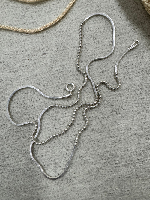 Sterling silver bead and snake chain necklace loosely coiled on grey stone, with the spring ring clasp near the centre of the frame.