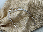 Sterling silver chain necklace resting on a woven jute pouch, showing a bead section running into a snake section beside the flat end tag.