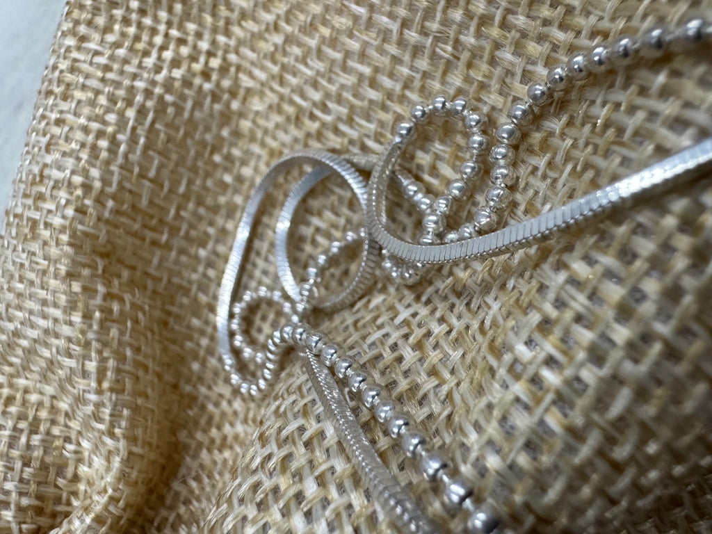 Close view of the sterling silver chain looped on jute, with a snake section curving in front of two runs of round beads.