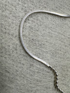 Close view of a snake section of the sterling silver chain necklace running into a row of round beads on grey felt.