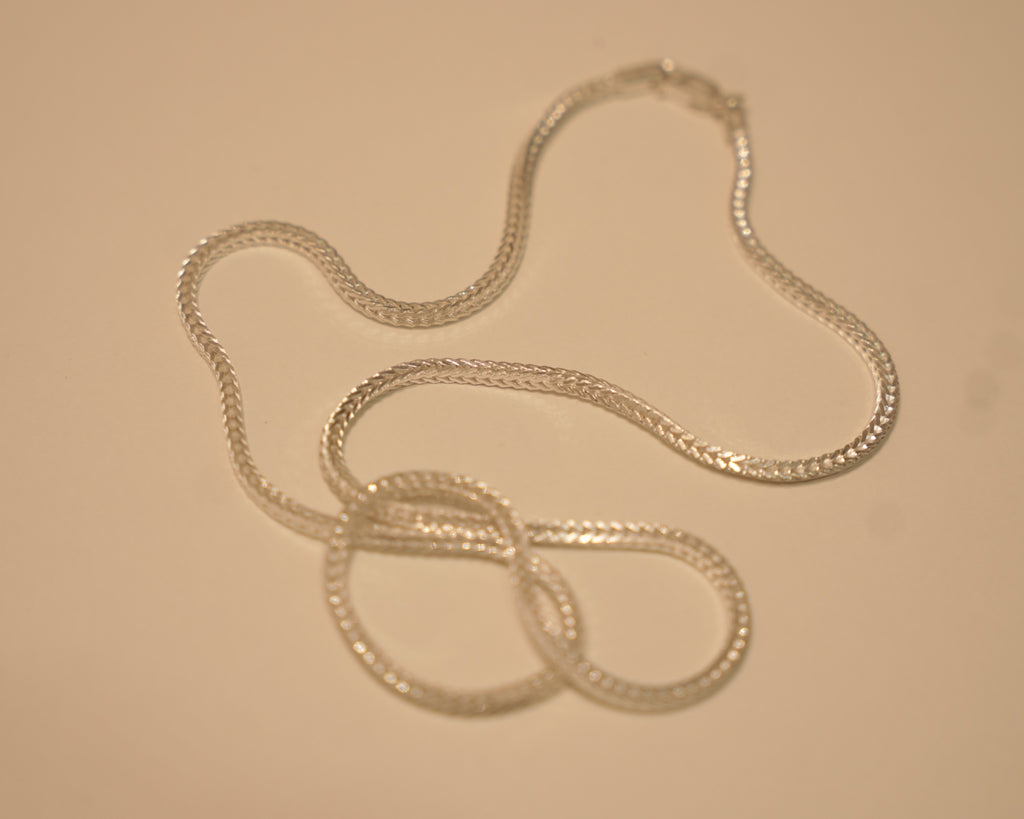 Sterling silver foxtail chain coiled loosely on a pale surface.