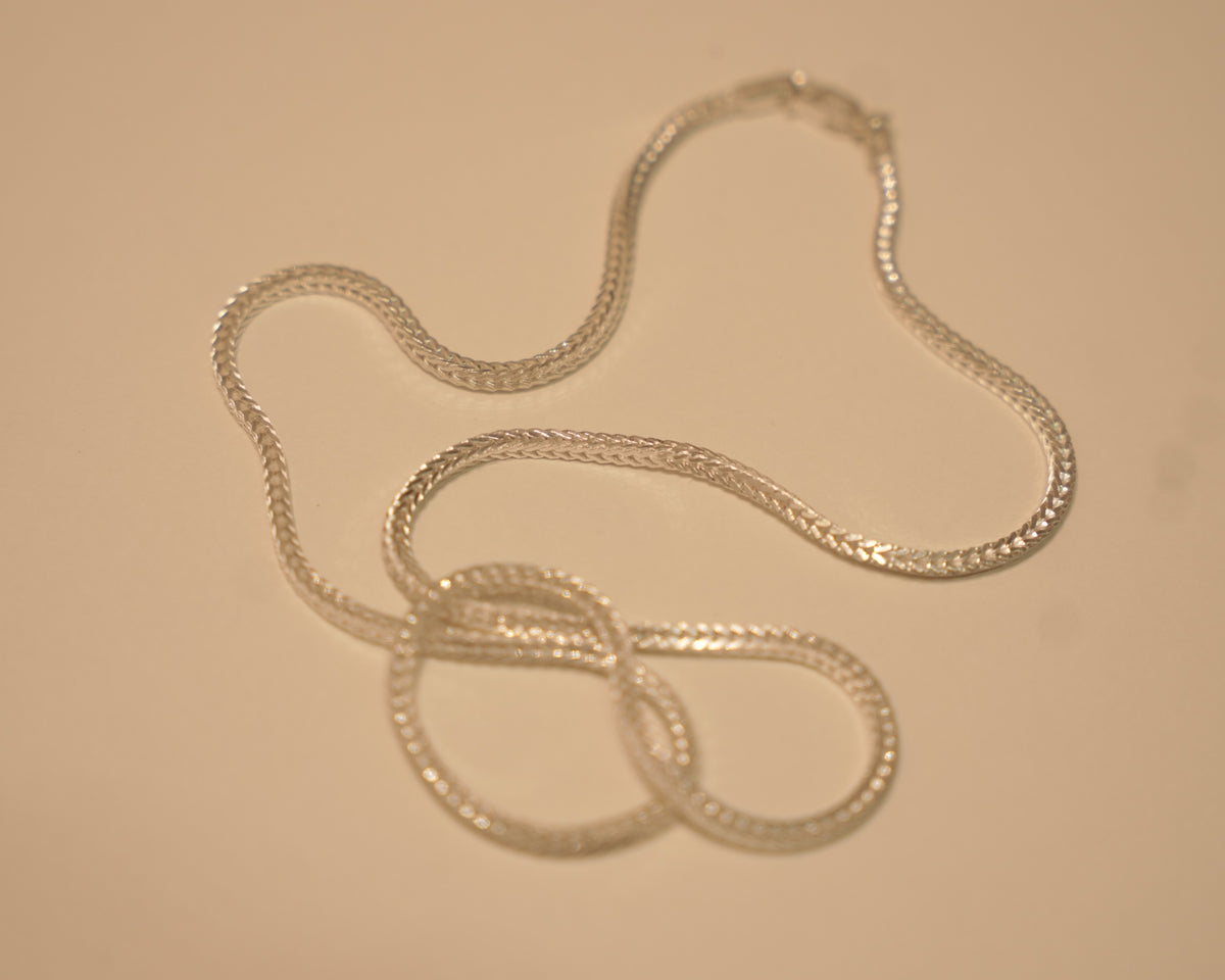Sterling silver foxtail chain coiled loosely on a pale surface.