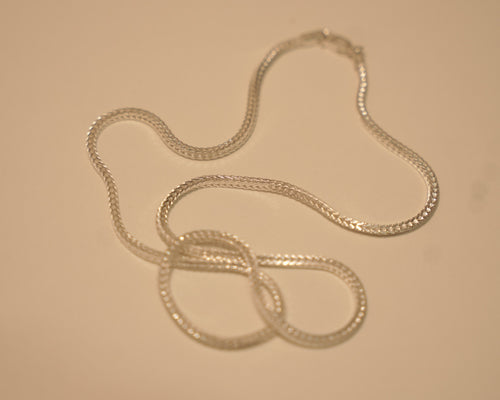 Sterling silver foxtail chain coiled loosely on a pale surface.