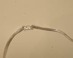Close view of the lobster clasp on the silver foxtail chain, with the silver mark stamped beside it.