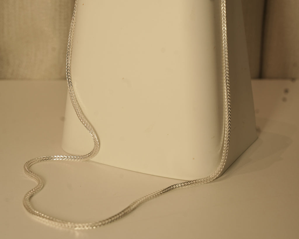 The silver foxtail chain draped over a white block, showing how it falls.
