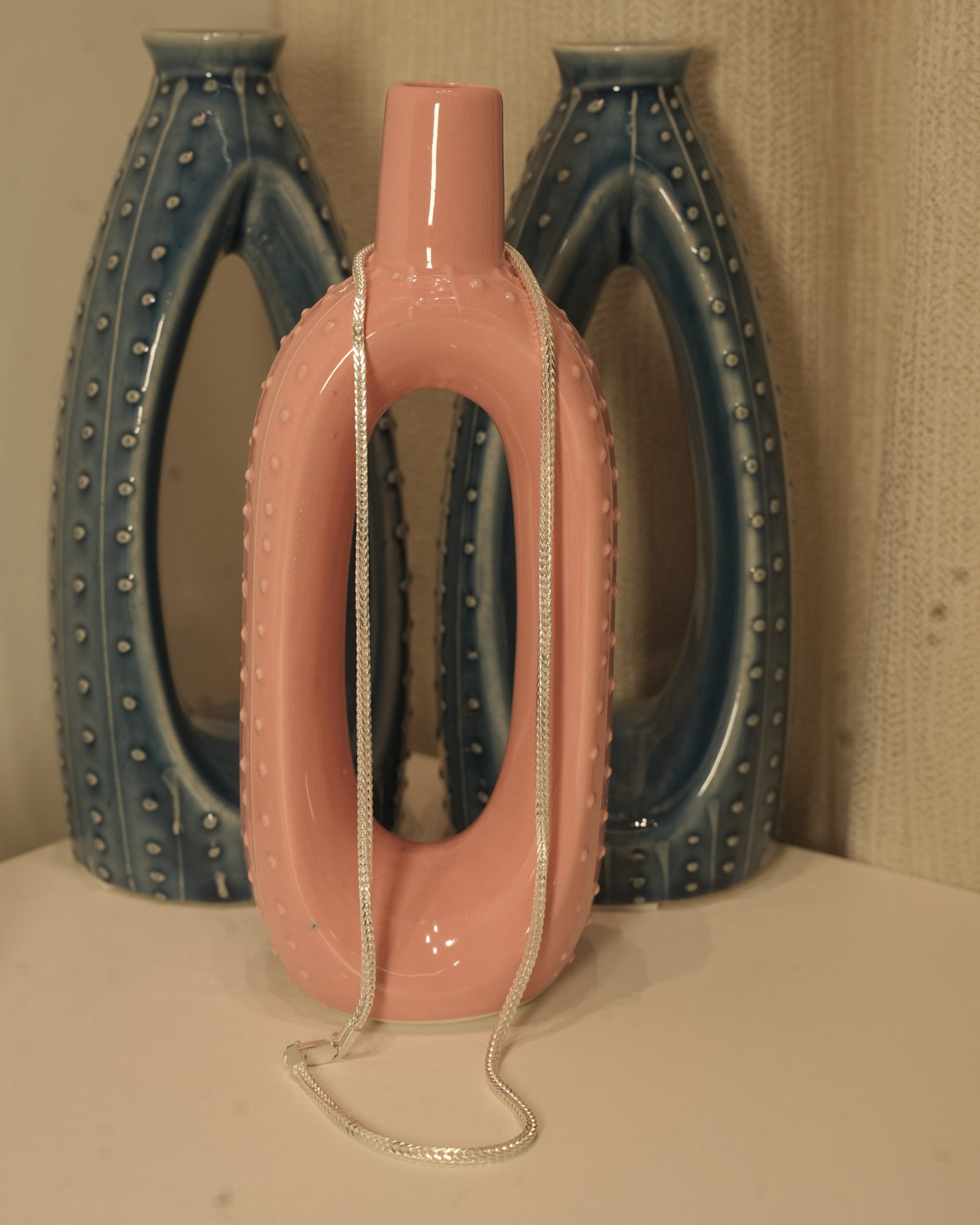 The silver foxtail chain hung over a pink and blue ceramic vase.