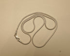 Sterling silver round snake chain coiled on a pale surface with the clasp to one side.