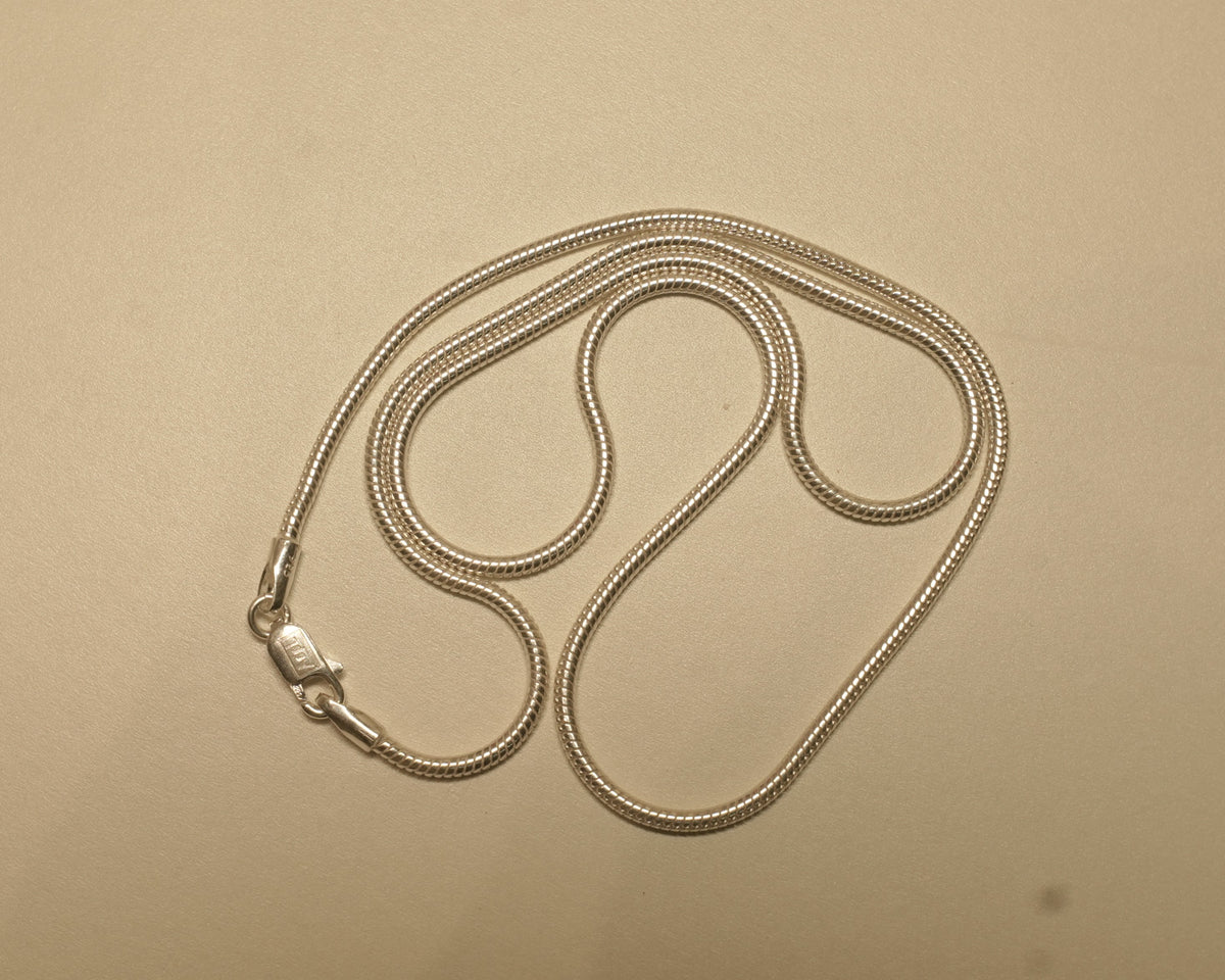 Sterling silver round snake chain coiled on a pale surface with the clasp to one side.
