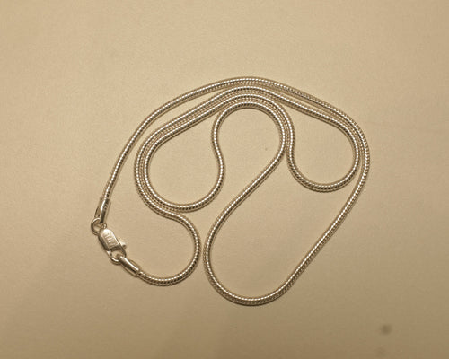 Sterling silver round snake chain coiled on a pale surface with the clasp to one side.
