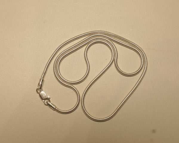 Sterling silver round snake chain coiled on a pale surface with the clasp to one side.
