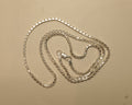 Sterling silver box chain coiled on a pale surface with the clasp at the centre.