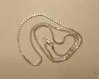 Sterling silver box chain coiled on a pale surface with the clasp at the centre.