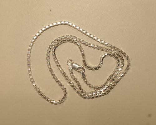 Sterling silver box chain coiled on a pale surface with the clasp at the centre.