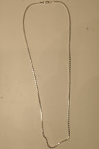 The silver box chain laid out in a long loop to show how it falls.