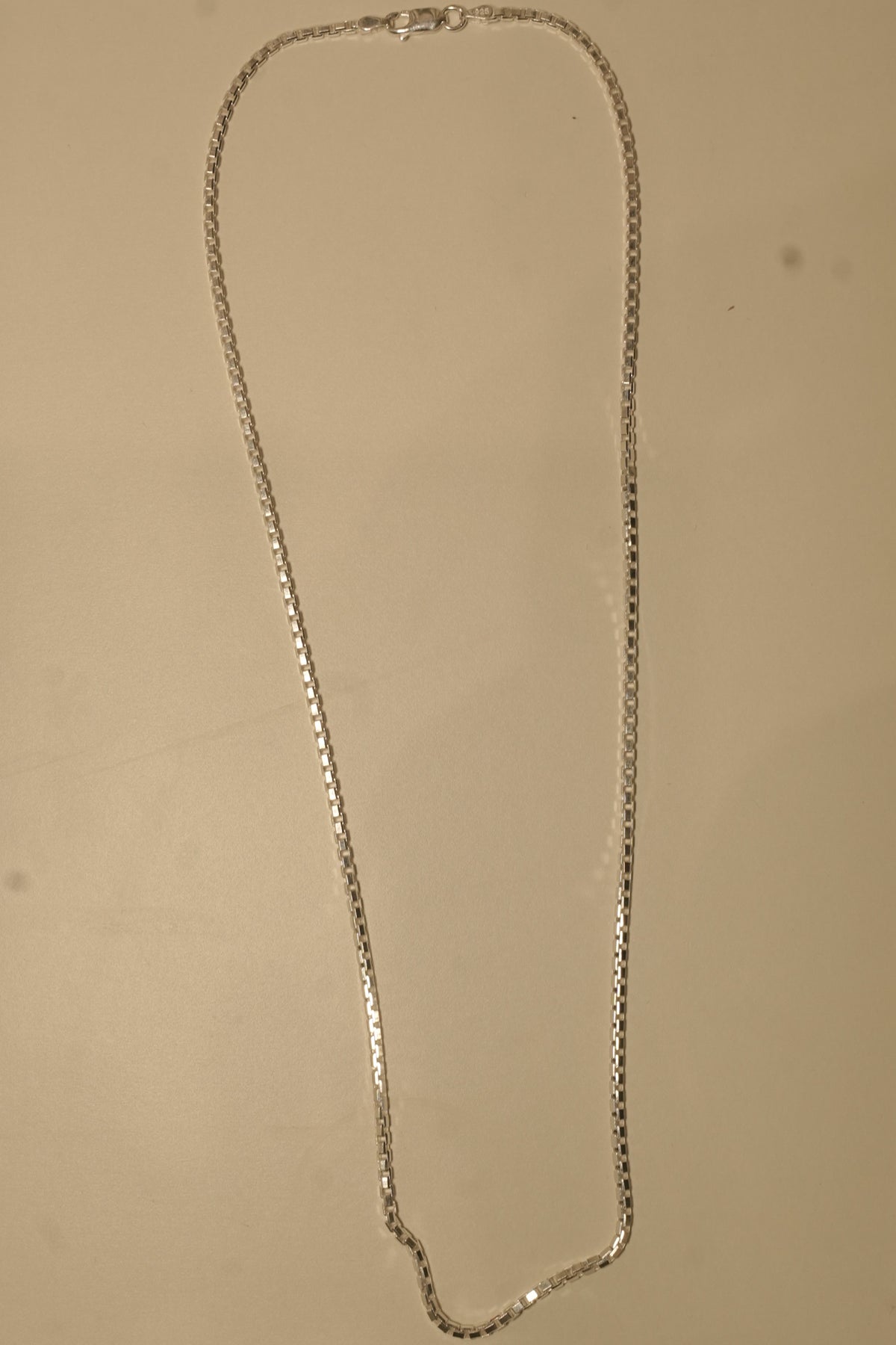 The silver box chain laid out in a long loop to show how it falls.