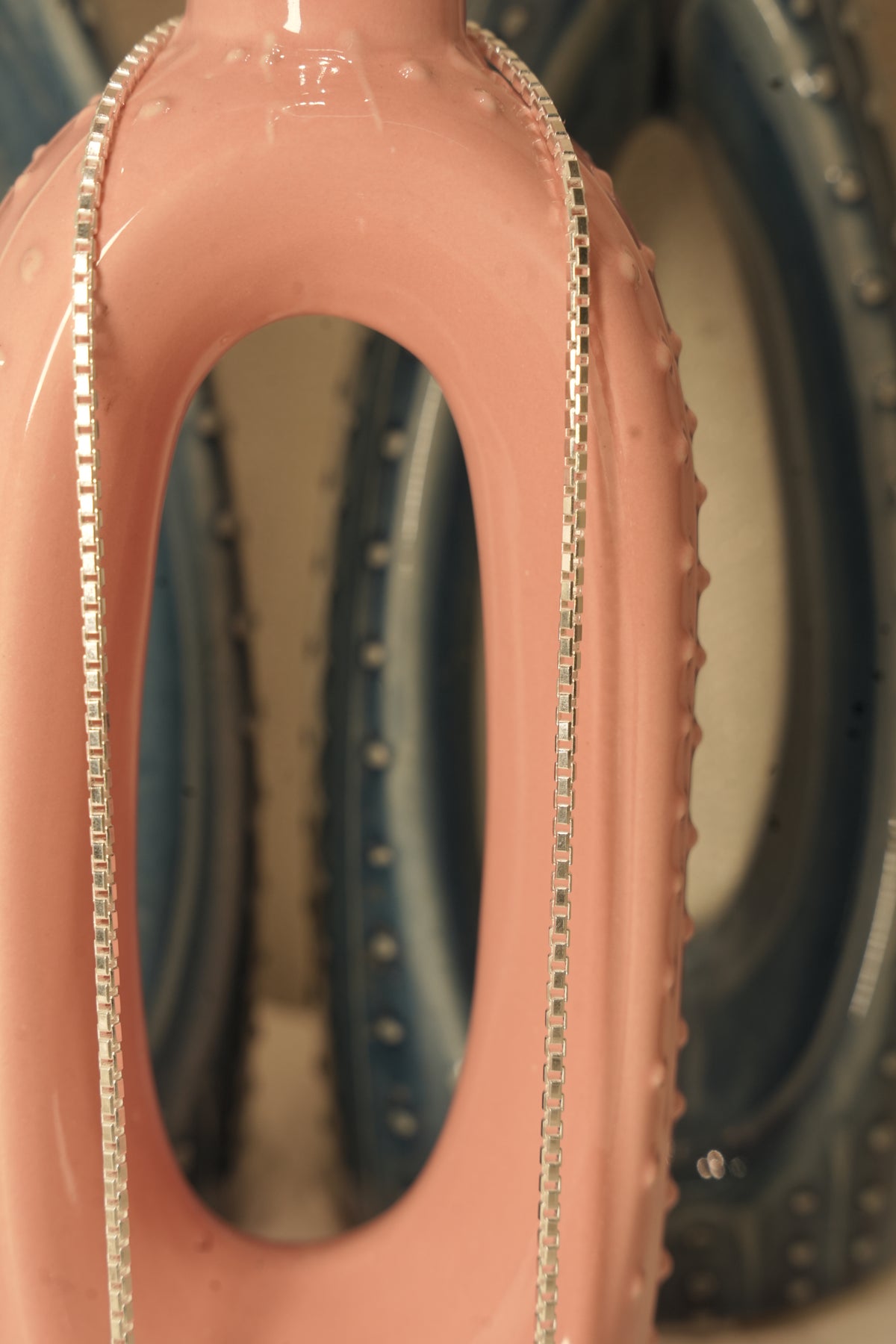 Close view of the silver box chain lying along the rim of a pink ceramic vase.