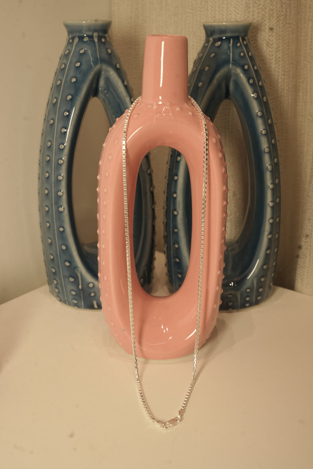 The silver box chain draped over a pink and blue ceramic vase.