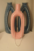 The silver box chain draped over a pink and blue ceramic vase.