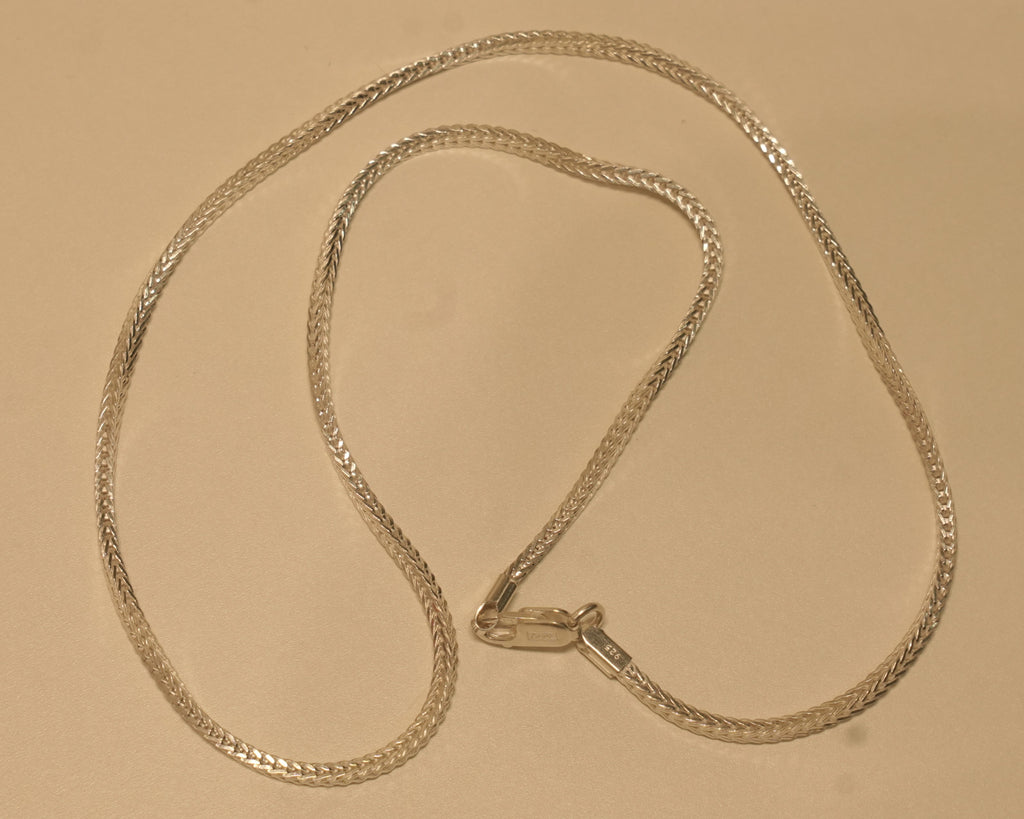Slim sterling silver foxtail chain coiled on a pale surface with the clasp at the centre.