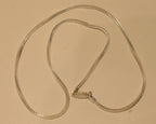 Slim sterling silver foxtail chain coiled on a pale surface with the clasp at the centre.