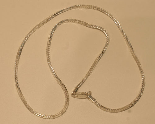 Slim sterling silver foxtail chain coiled on a pale surface with the clasp at the centre.