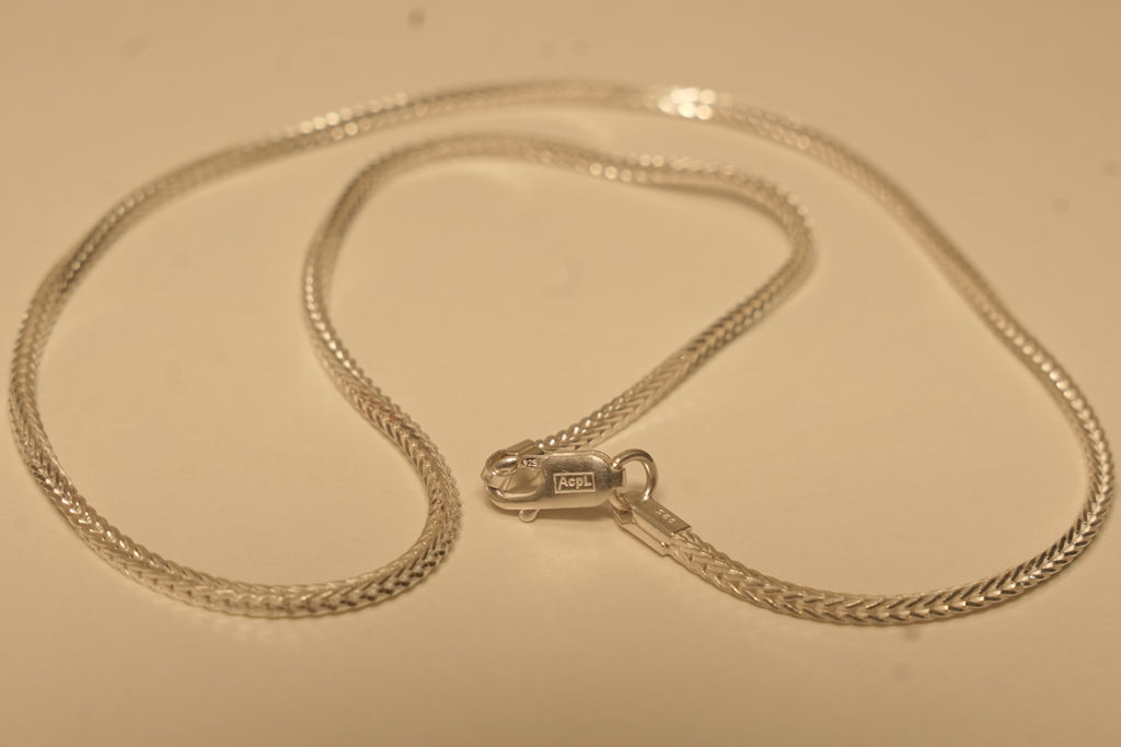 The slim silver foxtail chain coiled with the lobster clasp lying open in the middle.