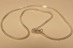 The slim silver foxtail chain coiled with the lobster clasp lying open in the middle.