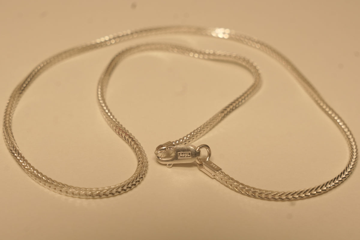 The slim silver foxtail chain coiled with the lobster clasp lying open in the middle.